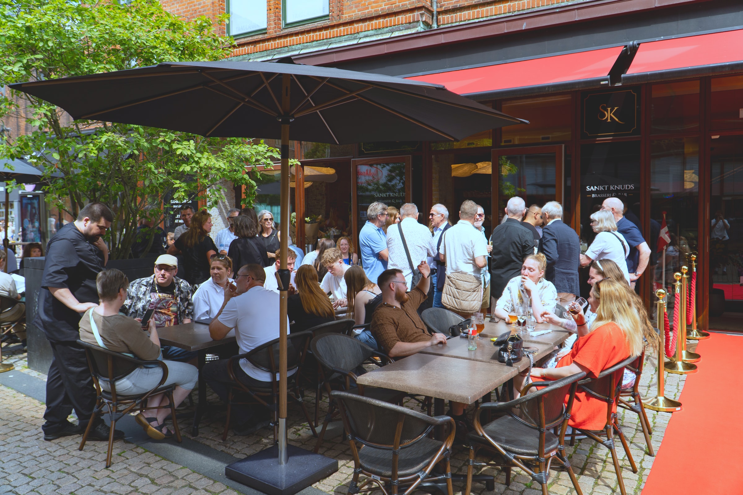 Gæster i solen på fortovsserveringen foran Sankt Knuds Brasseri & Bar i Ryesgade